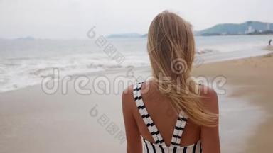 一个年轻的微笑女人，穿着黑色和白色的裙子，独自走在热带海滩上，在背景上看着相机